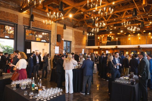 Crowd of professionals networking at a large indoor business event with exposed brick walls, wood beams and hanging lights.