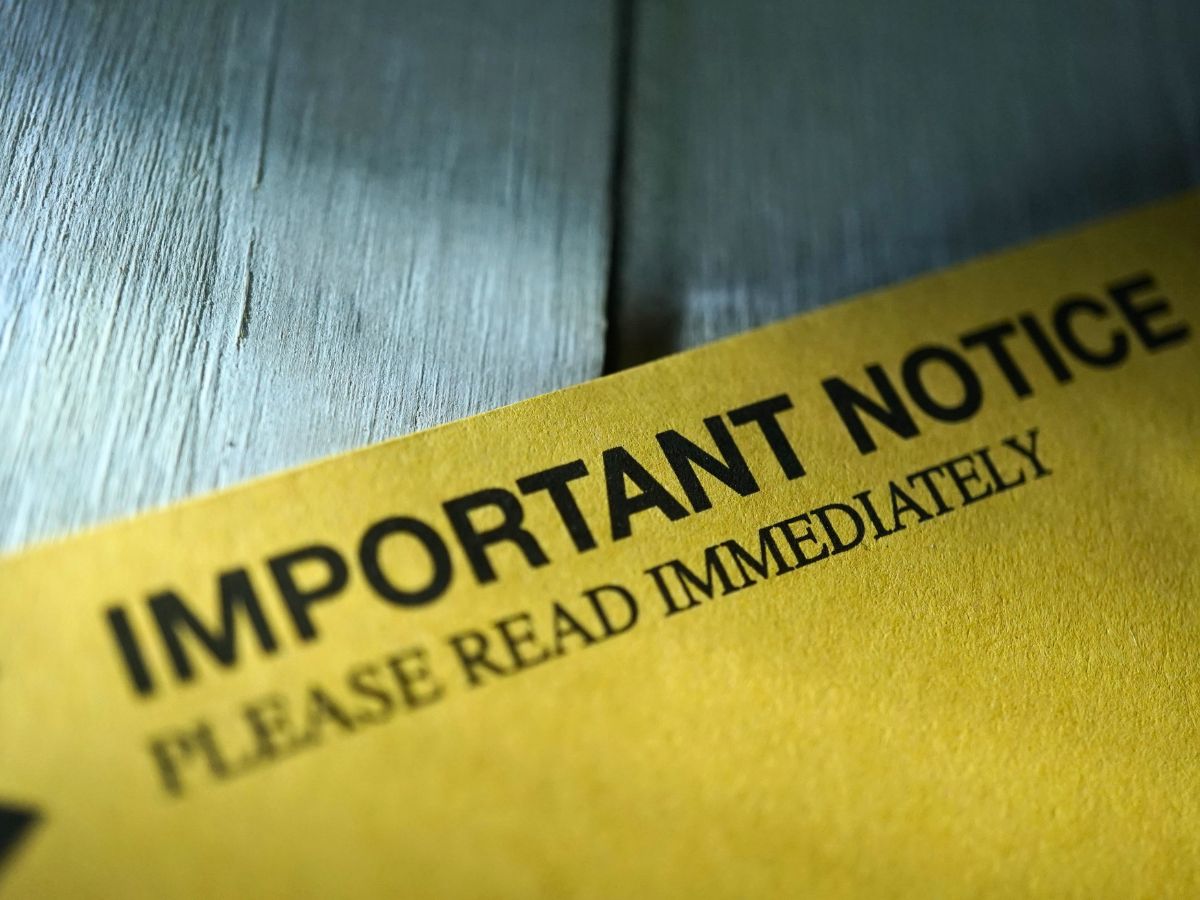 A yellow envelope or document on a weathered gray wooden surface printed with the words "Important Notice — Please Read Immediately."