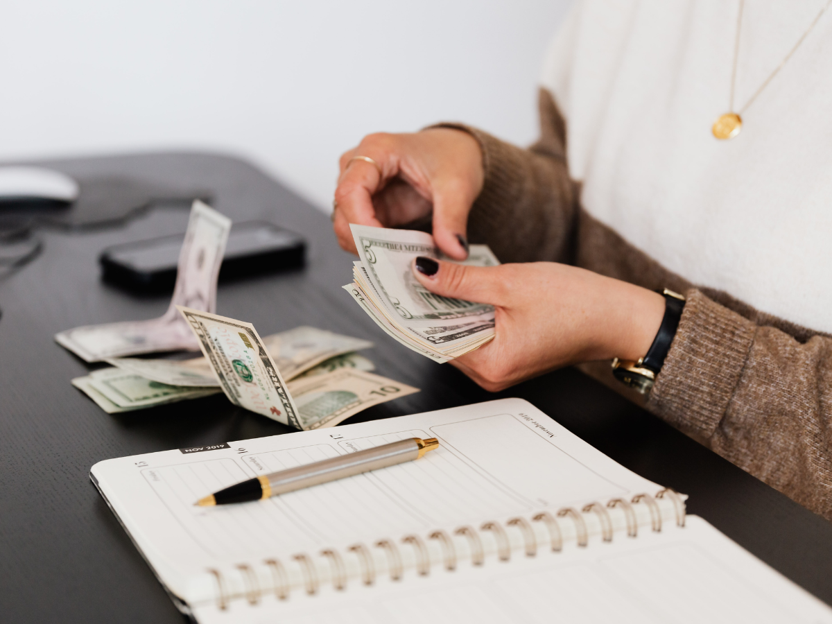 Claude responded: A person counting US currency by hand over a dark desk, with a spiral notebook, pen, phone and computer mouse nearby.A person counting US currency by hand over a dark desk, with a spiral notebook, pen, phone and computer mouse nearby.
